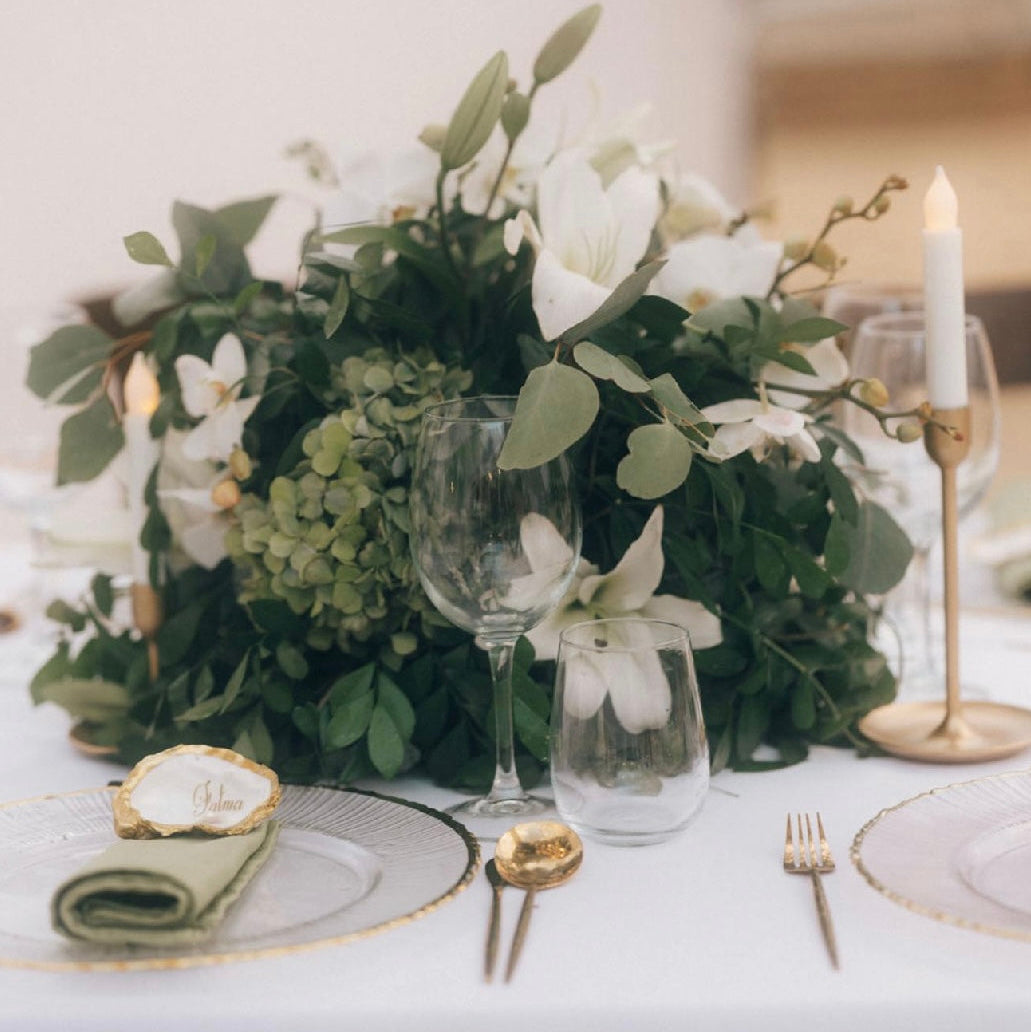 Elegant table setting with floral arrangement, glasses, and candles on a white tablecloth.