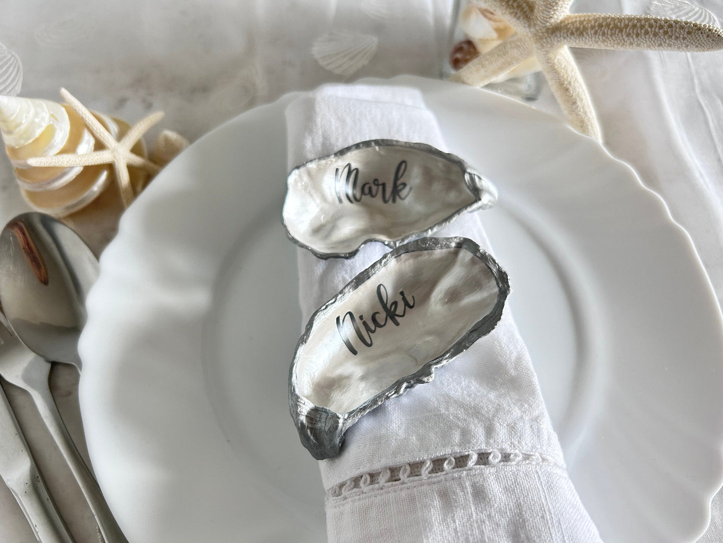 Two oyster shells with silver edges. The shells are placed on a white napkin with the names &#39;Mark&#39; and &#39;Nicki&#39; written in black on the inside of the shells.