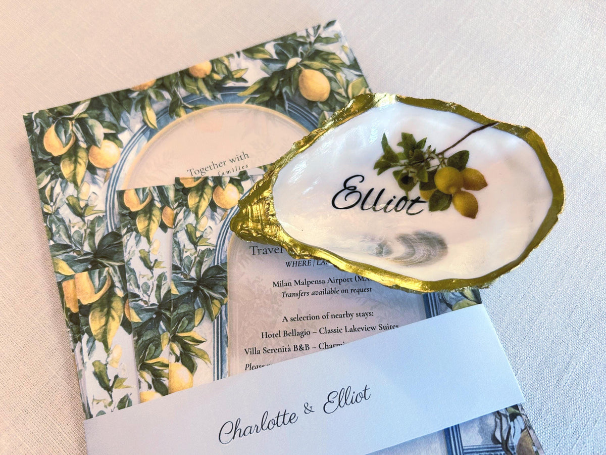 A matching  oyster shell with gold edging, personalised with a name and a lemon sprig. It sits atop a this invitation set  and matches perfectly for name places to elevate your wedding or event.