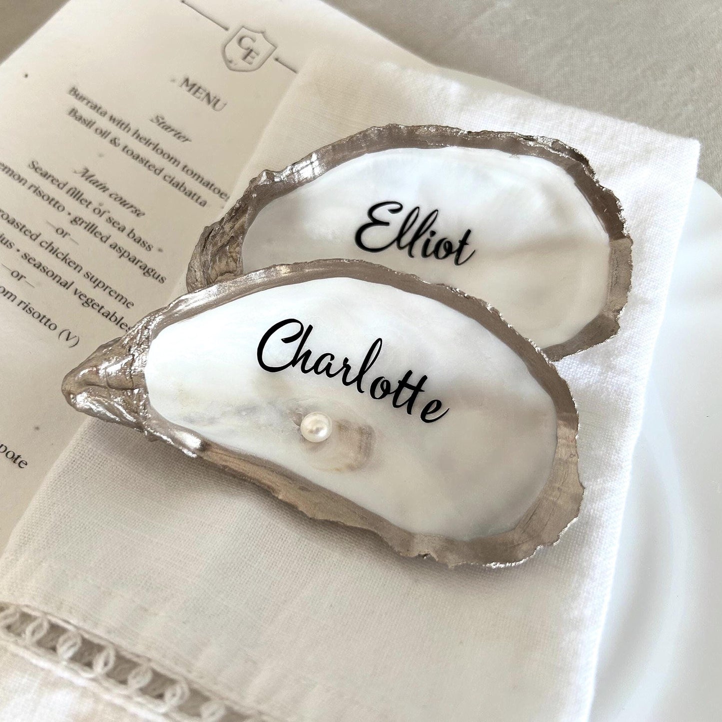 a oyster shell place cardd with champagne god  edging, inscribed with the names  A small pearl is nestled in these shells although optional.