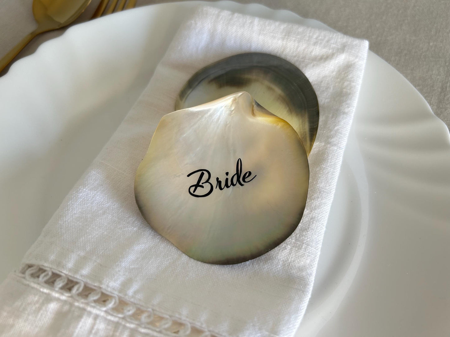 A pearlescent black lip seashell place card with the word "Bride" in elegant script, perfect for a wedding or special occasion