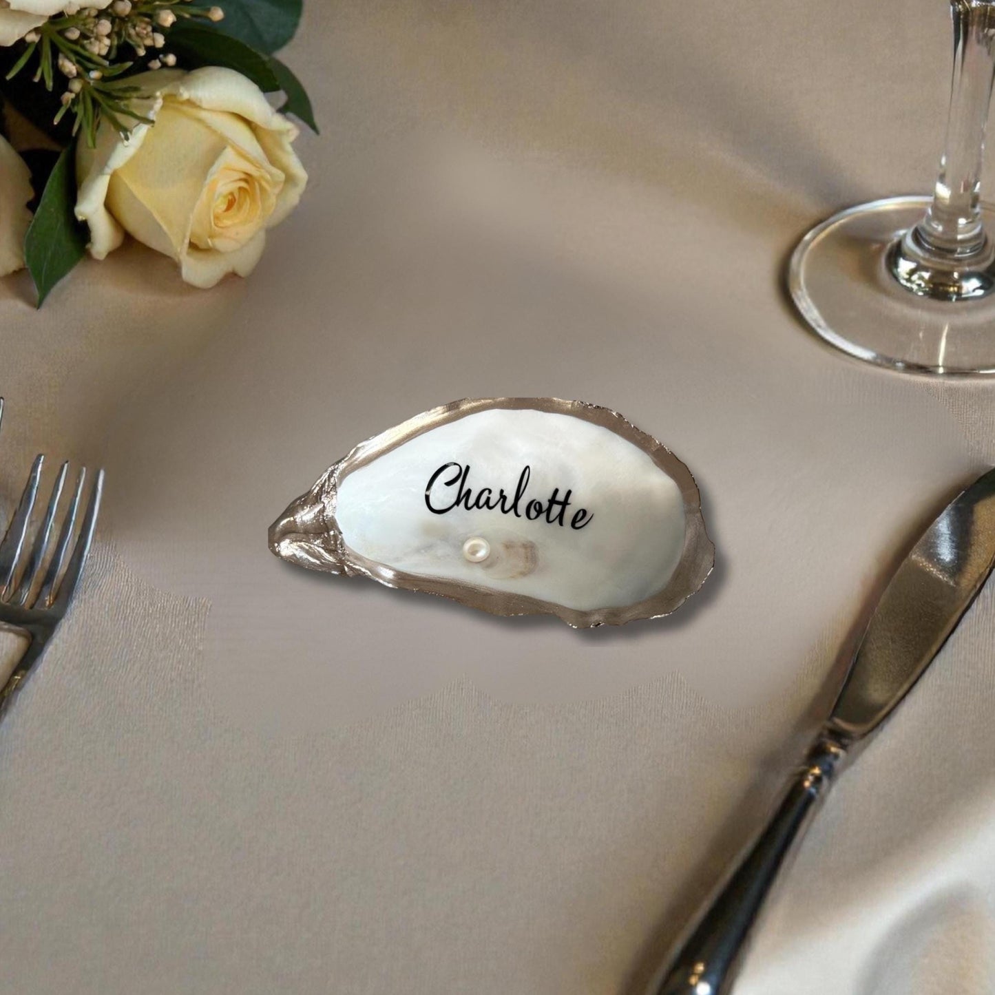 A natural white oyster shell place card holder with the name  in black script. A small pearl is under the name.